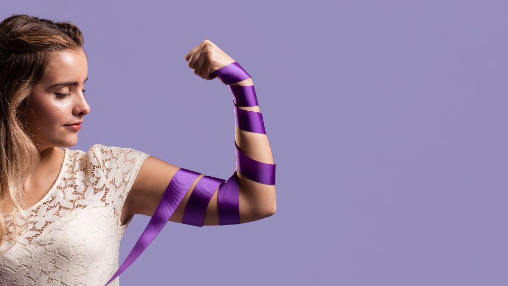 A woman flexing her arm while tying a purple ribbon around it