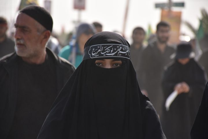 A woman wearing a black burqa and niqab with Arabic text written on it